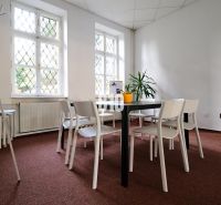 Interior of an office with white chairs, a table, and a plant on the carpet.
