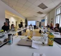 People in the office are discussing at a large table, with a presentation and refreshments.
