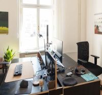 Offices with two computer workstations, a plant, and paintings on the walls.