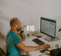 A man is working on a computer in an office, surrounded by technology and notes.