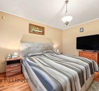 Bedroom in a family house with a bed, television, and wooden decor flooring.