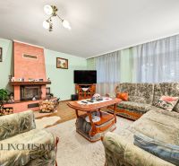 Living room in a family house with a fireplace, floral sofa set, and wooden decor flooring.