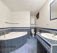Bathroom in a family house with a corner bathtub, sink, toilet, and blue tiles.