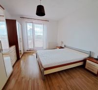 A bright bedroom in a two-room apartment with a wooden decor floor and large windows.