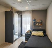 A bedroom in a three-room apartment with dark furniture, a shelf, and a floor with a wooden decor.