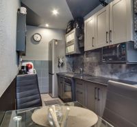 A kitchen in a 3-room apartment with dark gray kitchen cabinets and a dining table with a glass top.