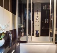 A bathroom in a 3-room apartment with a bathtub and a shower box, complemented by artificial flowers.