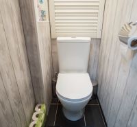 A toilet in a 3-room apartment with wood decor on the walls and a black floor.