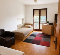 A room in a 3-room apartment with beds, a chair, a carpet, and a floor with a wooden decor.