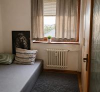 A room in a 3-room apartment with a bed, curtains, and a carpet on a floor with a wooden decor.