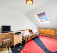 Attic room in a family house with a desk, sofa, and colorful carpet.