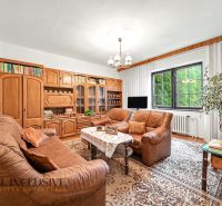 Living room in a family house with a leather sofa, shelving unit, and a window overlooking the green exterior.