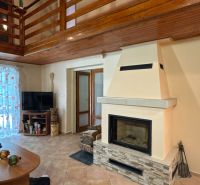 Interior of a cabin with a fireplace and a gallery, wooden decor flooring and a TV corner.