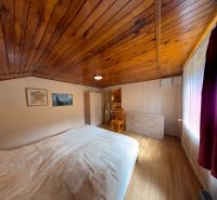A room in a cottage with a wooden ceiling, a floor with a wooden decor, furniture, and a bed.