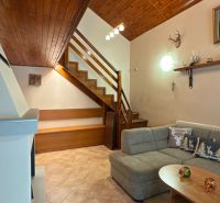 Interior of a cabin with a wooden floor, a sofa, a staircase, and decorations.