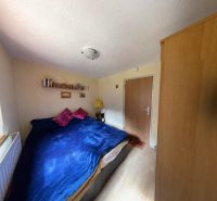 Room in a cottage with a bed, decorated floor, warm lighting, and furniture.