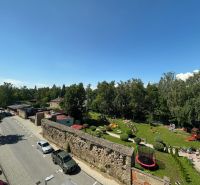 A street with cars and a wall near the park in Kežmarok, offices close to greenery.