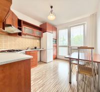 A kitchen in a 2-room apartment with a wooden decor floor, a dining table, and appliances.