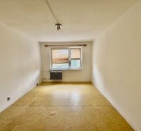 A room in a 2-room apartment with a beige floor and a window with a radiator.