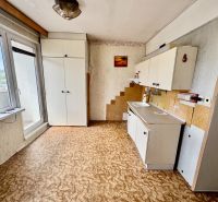 A kitchen in a 2-room apartment with white furniture and a wooden decor floor.