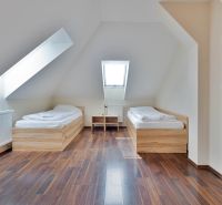 Two beds, a slanted roof, and a floor with a wooden decor in a 2-room apartment.