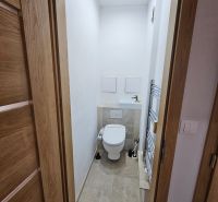 Compact toilet with ceramic tiles and a white sink in a 2-room apartment.