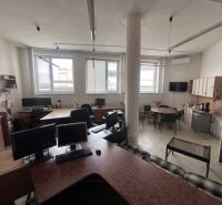 In an office with a wooden decor floor, there are desks, computers, and a kitchenette.