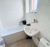 A bathroom with a bathtub, sink, and toilet, tiled with light tiles.