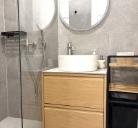 A bathroom in a 3-room apartment with a sink on a wooden cabinet and a round mirror.