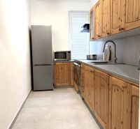 A kitchen with wooden cabinets, a white wall, and light tiles in a three-room apartment.