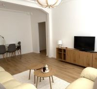 Living room of a three-room apartment with a wooden decor floor, a sofa, and a dining table.