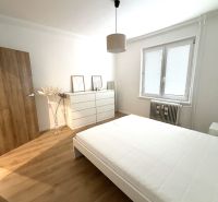 A bedroom with light walls, a bed, and a floor with a wood decor in a 3-room apartment.