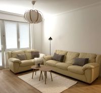 A bright living room with cream sofas, a carpet, and a wooden decor floor.