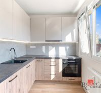 A kitchen of a 2-room apartment with large windows and a countertop with a wooden decor.