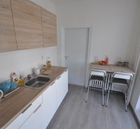 A kitchen with a wood-patterned floor in a 2-room apartment, with a dining table and chairs.