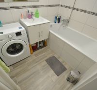 A bathroom in a 2-room apartment with a bathtub, washing machine, and cabinet.