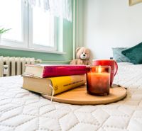 A cozy bedroom with books, a candle, and a plush bear on the bed in a 2-room apartment.