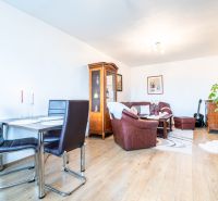 Living room of a two-room apartment with a wooden decor floor, leather sofa, and dining table.