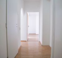 A hallway with a wooden decor floor and white walls in a 2-room apartment.