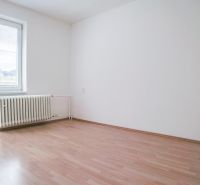 A room in a 2-room apartment with a wooden decor floor, white wall, radiator.