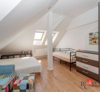 Attic room with a bed, chair, and wooden decor flooring in a 3-room apartment.