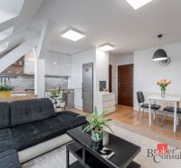 Living room with wood-patterned flooring and a kitchenette in a three-room apartment.