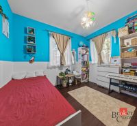 A children's room with colorful walls, a bed, a piano, and shelves full of toys and books.