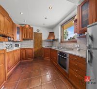 A kitchen in a family house with a ceramic floor, wooden cabinets, and a large window.