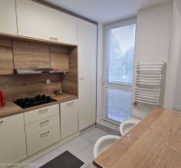 A kitchen in a 3-room apartment with a wooden decor floor and light cabinets.