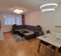 Living room with a corner sofa, dining table, and wood-patterned flooring in a three-room apartment.