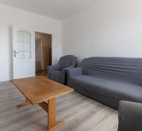 Living room with a sofa, an armchair, a wooden table, and a wooden-patterned floor in a 3-room apartment.