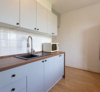 A kitchen with white cabinets, a sink, a microwave, and a wood-patterned floor.