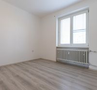 An empty room with a window, a wooden decor floor, and a radiator in a 3-room apartment.
