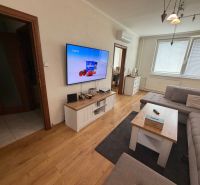 Living room with wood-patterned flooring, gray sofa, and television, in a three-room apartment.